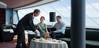 Una pareja disfruta de un té de la tarde servido por un mayordomo en el elegante Top Sail Lounge con vistas panorámicas al mar | MSC Cruceros