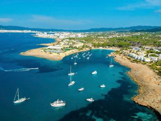 A picturesque view of Port de Torrent Beach in Ibiza showcasing clear waters, sandy shores, and lush greenery | MSC Cruises