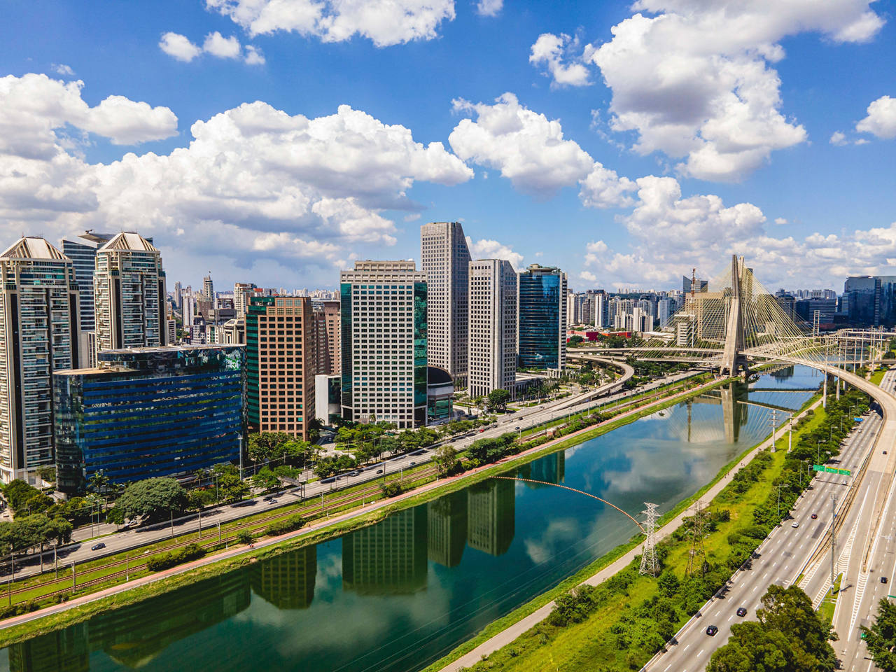 Eine lebendige Stadtansicht mit modernen Wolkenkratzern neben einem ruhigen Fluss und üppigem Grün unter einem strahlend blauen Himmel | MSC Cruises