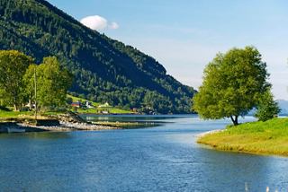 Eine friedliche Landschaft mit einem ruhigen Fluss, umgeben von üppigem Grün und Bergen unter einem strahlend blauen Himmel | MSC Cruises