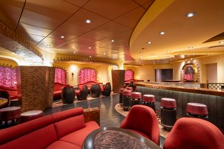 A welcoming lounge area with red seating, tables, and warm lighting on MSC Fantasia | MSC Cruises