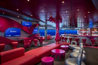 A vibrant seating area in the Liquid Disco, featuring tables, armchairs, and a bar counter overlooking the sea | MSC Cruises