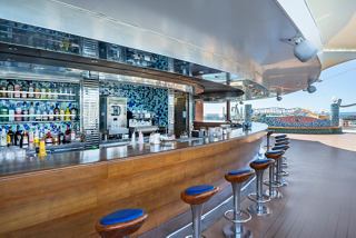 A welcoming outdoor bar area with wooden counter and seating, perfect for enjoying drinks in the sun | MSC Cruises