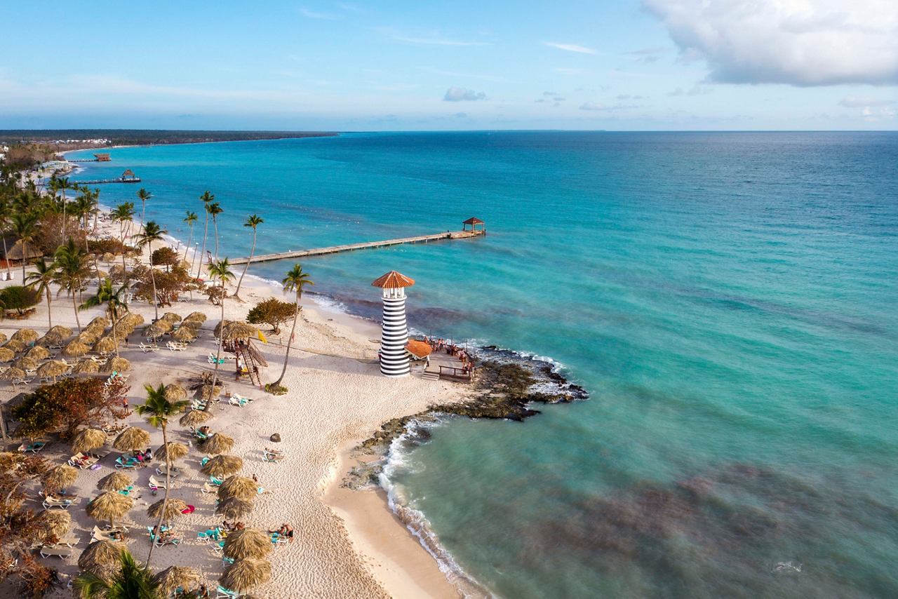 A tranquil beach in La Romana featuring a lighthouse, palm trees, and sunbeds by the sparkling Caribbean Sea | MSC Cruises