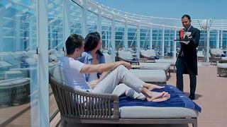 A couple enjoys a relaxing moment at The One Pool in the MSC Yacht Club while being served by a friendly staff member | MSC Cruises