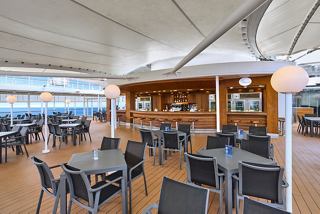 A spacious outdoor sitting area with tables and chairs, featuring the Il Girasole Bar, overlooking the sea | MSC Cruises