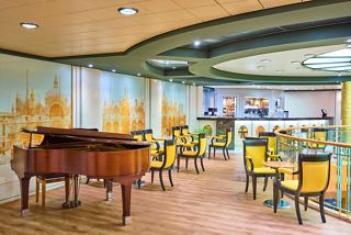 A warm and inviting sitting area featuring a piano, tables, and chairs at Caffè San Marco on MSC Armonia | MSC Cruises