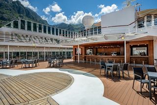 An inviting outdoor bar area with seating, surrounded by mountains and a clear sky | MSC Cruises