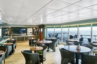 A modern dining area with tables and chairs, featuring large windows overlooking the sea | MSC Cruises