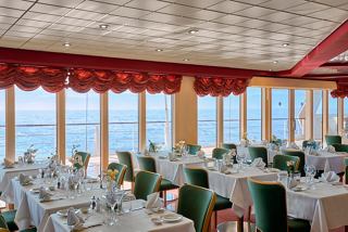 Elegant dining area with tables set for guests, featuring a view of the sea through large windows | MSC Cruises