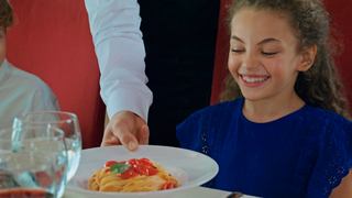 Un serveur sert une délicieuse assiette de spaghetti aux tomates à une jeune fille dans un restaurant familial | MSC Croisières
