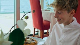 A child enjoys a delicious plate of risotto while seated at a restaurant table with a view | MSC Cruises