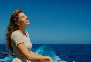 A woman enjoys the expansive sea view from the deck of the MSC Sinfonia, surrounded by a clear blue sky | MSC Cruises