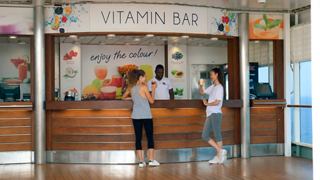 Two women enjoy refreshing drinks at the Vitamin Bar with a friendly crew member serving them | MSC Cruises