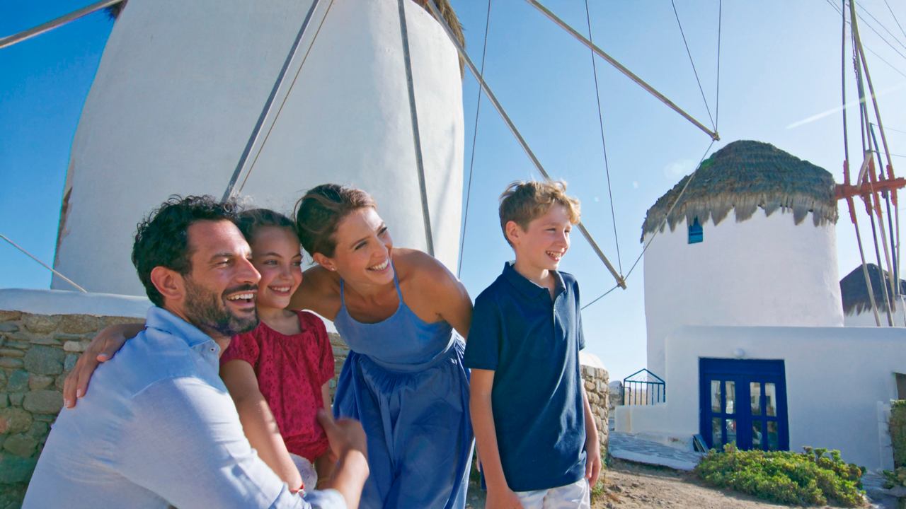 Eine Familie genießt einen Moment zusammen bei einer traditionellen Windmühle in Mykonos unter einem klaren blauen Himmel | MSC Cruises