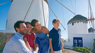 A family enjoys a moment together near a traditional windmill in Mykonos under a clear blue sky | MSC Cruises