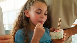 A child is enjoying ice cream from a cup while being lovingly supported by an adult | MSC Cruises