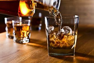 Whiskey being poured over ice in a glass, with additional drinks in the background | MSC Cruises