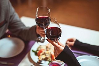 Two glasses of red wine are raised in a toast above a beautifully set table with a delicious meal | MSC Cruises