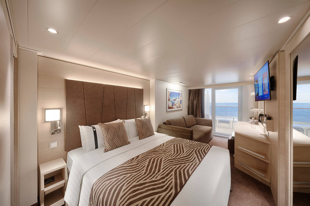 A stylish and comfortable cabin featuring a double bed, vanity area, sofa bunk bed, and a balcony with outdoor furniture | MSC Cruises
