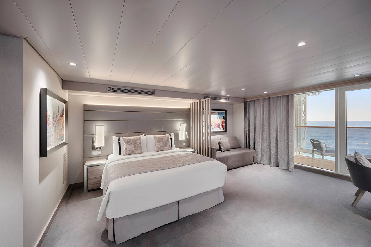 A spacious Grand Suite Aurea with terrace featuring a double bed, armchair, and outdoor furniture overlooking the sea | MSC Cruises