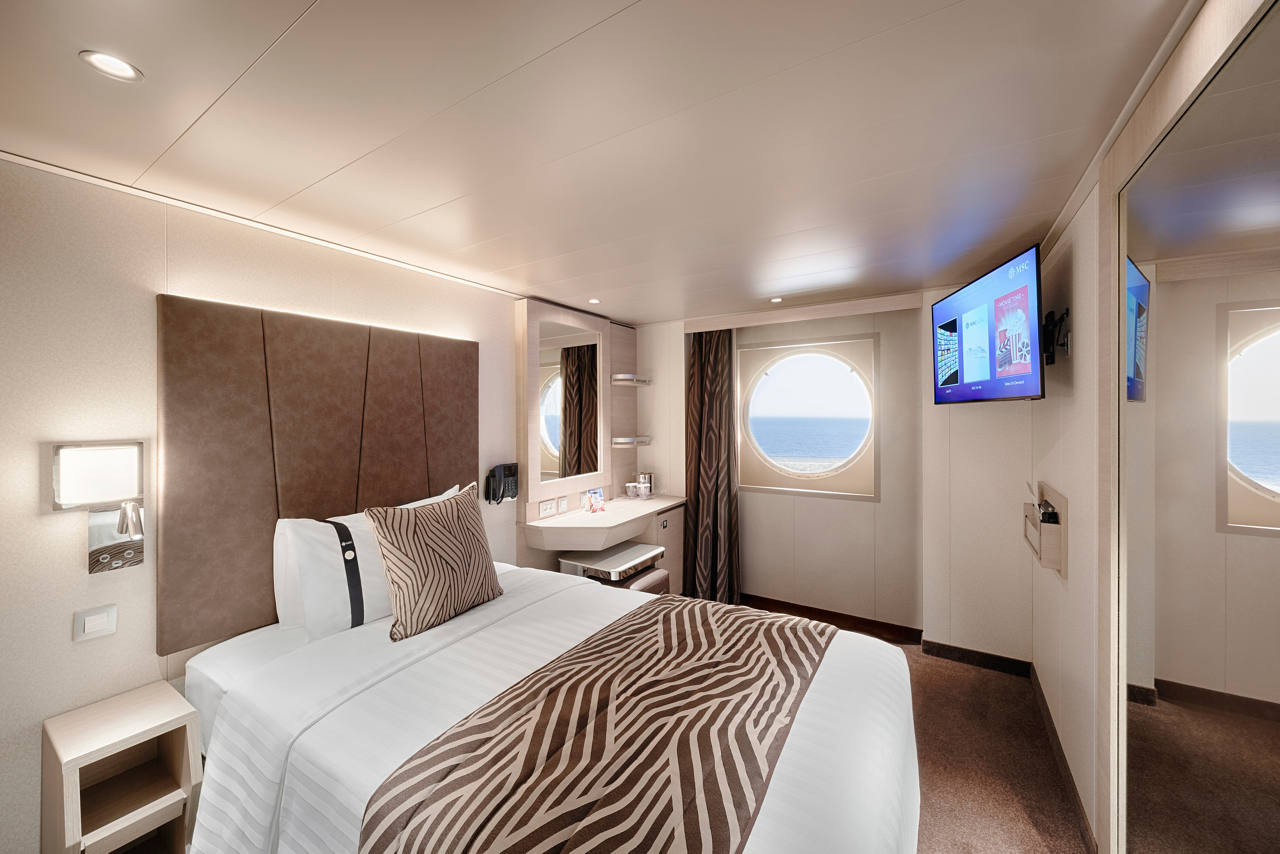 A spacious ocean view cabin featuring a double bed, vanity area, and porthole for natural light | MSC Cruises