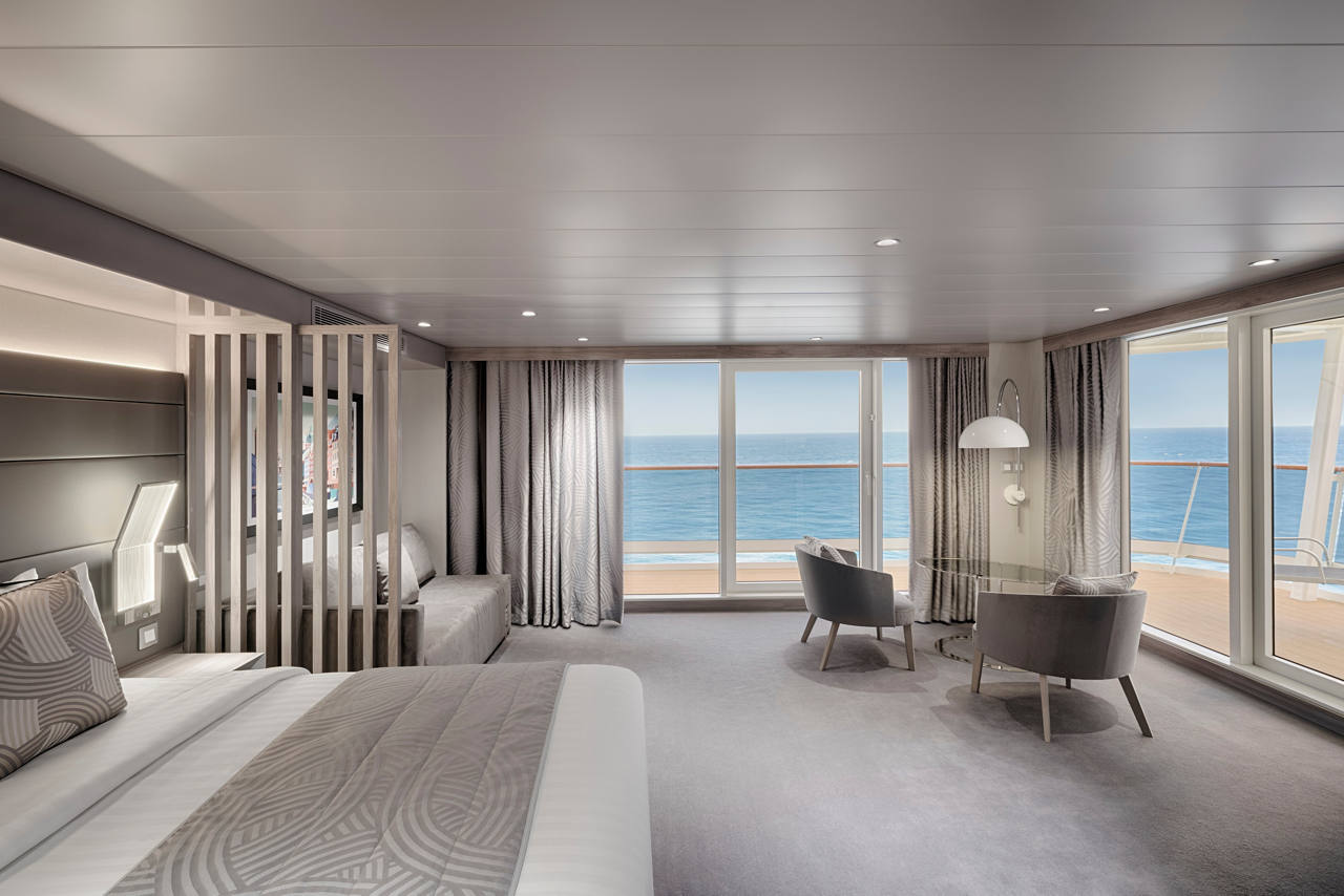 A spacious Grand Suite Aurea with a terrace featuring a double bed, seating area, and stunning sea views | MSC Cruises