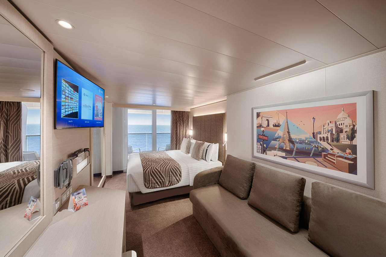 Deluxe balcony cabin featuring a double bed, sofa bed, and outdoor furniture with partial sea view | MSC Cruises