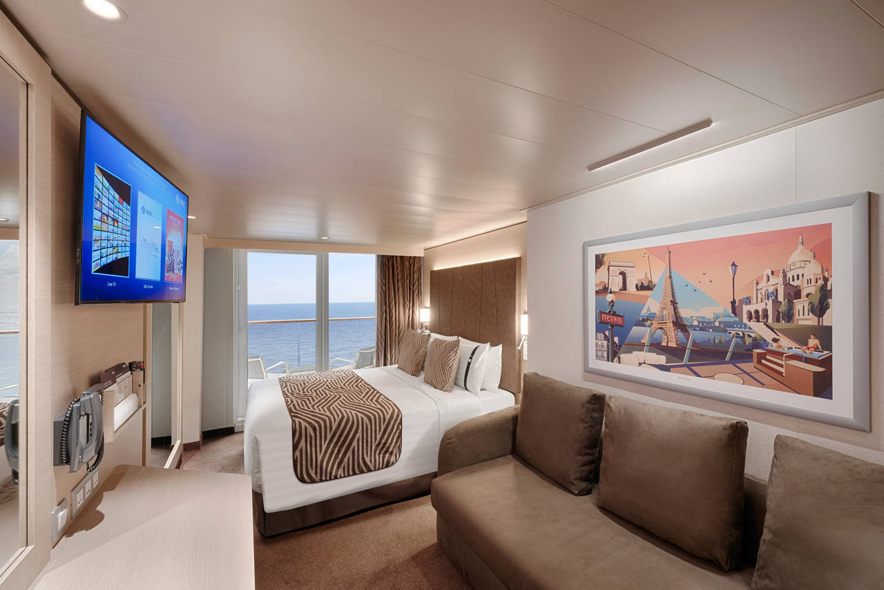 A spacious deluxe balcony cabin featuring a double bed, sofa bed, and a welcoming vanity area | MSC Cruises