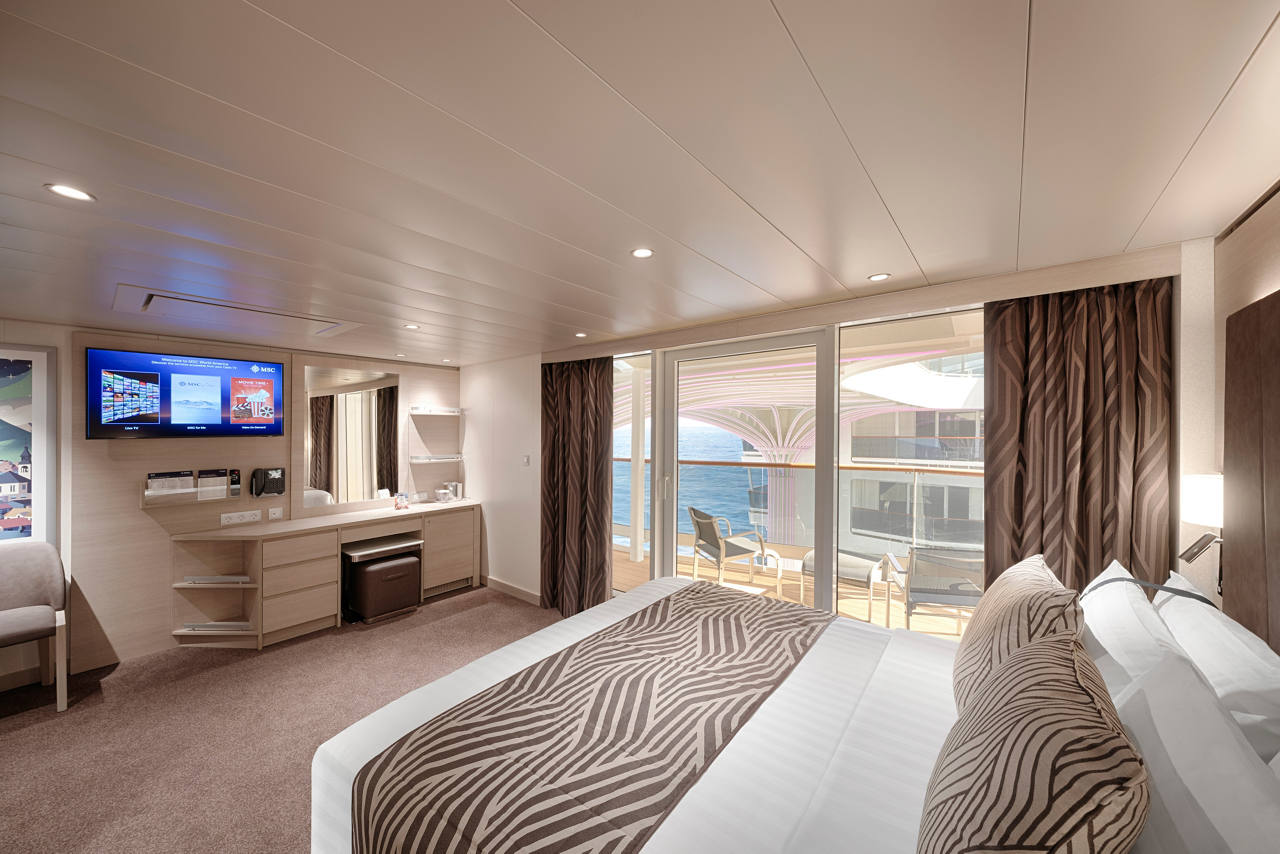 A warm and inviting Junior Suite Aurea featuring a double bed, vanity area, and a balcony with ocean views | MSC Cruises