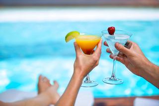 Two hands holding vibrant cocktails beside a sparkling pool, inviting relaxation and enjoyment | MSC Cruises