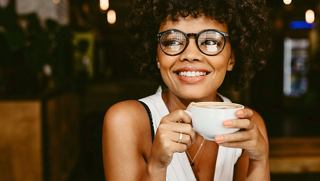 A woman enjoys a cappuccino in a warm café setting, radiating joy and connection | MSC Cruises