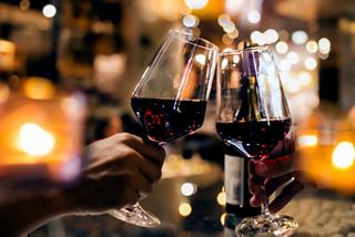 Two glasses of red wine clink together in a celebratory toast amidst a warm, inviting atmosphere | MSC Cruises