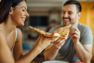 A couple sharing a slice of pizza in a warm, inviting atmosphere on board MSC Opera | MSC Cruises
