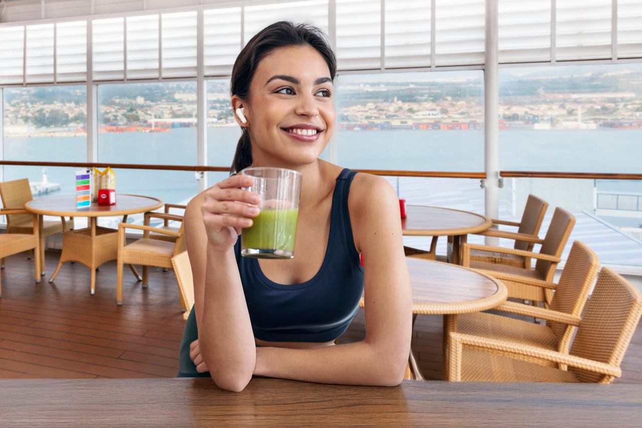 A woman enjoys a refreshing smoothie at the Vitamin Bar aboard MSC Armonia with a scenic view in the background | MSC Cruises