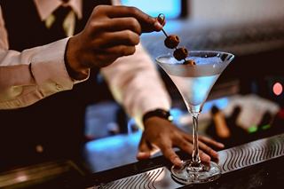 A bartender preparing a cocktail with a glass and olive, showcasing skill and attention to detail | MSC Cruises