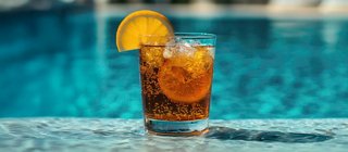 A refreshing cocktail garnished with an orange slice, served by a shimmering pool | MSC Cruises