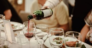 A waiter pouring red wine at a dining table, enhancing the dining experience at Oleandro Restaurant | MSC Cruises