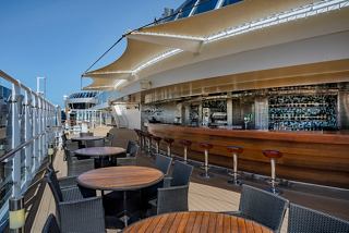 A welcoming outdoor bar area on MSC Splendida, featuring tables and chairs under a bright blue sky | MSC Cruises