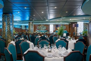 A welcoming dining area with teal chairs and tables set for guests at the Villa Verde Restaurant onboard MSC Splendida | MSC Cruises