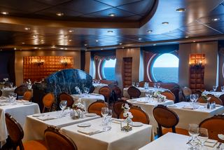 Elegant dining setup in La Reggia Restaurant aboard MSC Splendida, with a view of the sea through large portholes | MSC Cruises