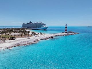 Vista aérea de una hermosa playa con un faro, palmeras y el barco MSC Seashore en el mar Caribe | MSC Cruceros