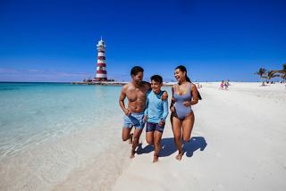 A joyful family enjoying a sunny day at the beach, with a lighthouse in the background and clear blue skies | MSC Cruises