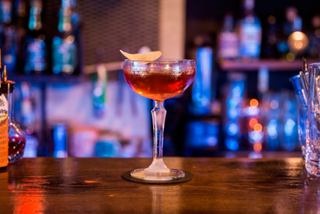 A vibrant cocktail served in a stylish glass, set against a backdrop of illuminated bottles | MSC Cruises