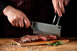 A chef skillfully slicing a steak on a wooden board garnished with rosemary | MSC Cruises