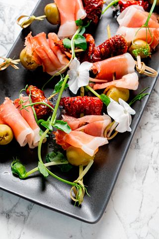 A close-up of a beautifully arranged platter of gourmet appetizers featuring ham and olives | MSC Cruises