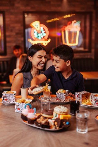 Una madre y su hijo comparten un momento alegre en una mesa llena de deliciosa comida en un restaurante vibrante | MSC Cruceros