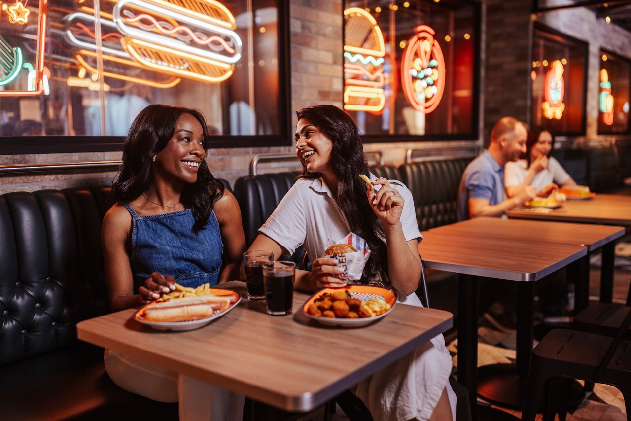 Two friends enjoy a meal together in a lively restaurant setting aboard MSC World America | MSC Cruises