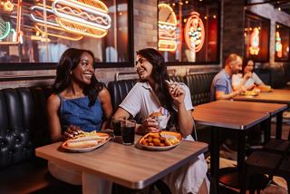 Two friends enjoy a meal together in a lively restaurant setting aboard MSC World America | MSC Cruises