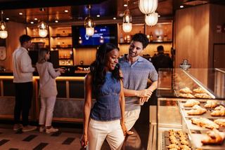 A couple enjoys a selection of pastries at a vibrant café, with other guests in the background | MSC Cruises